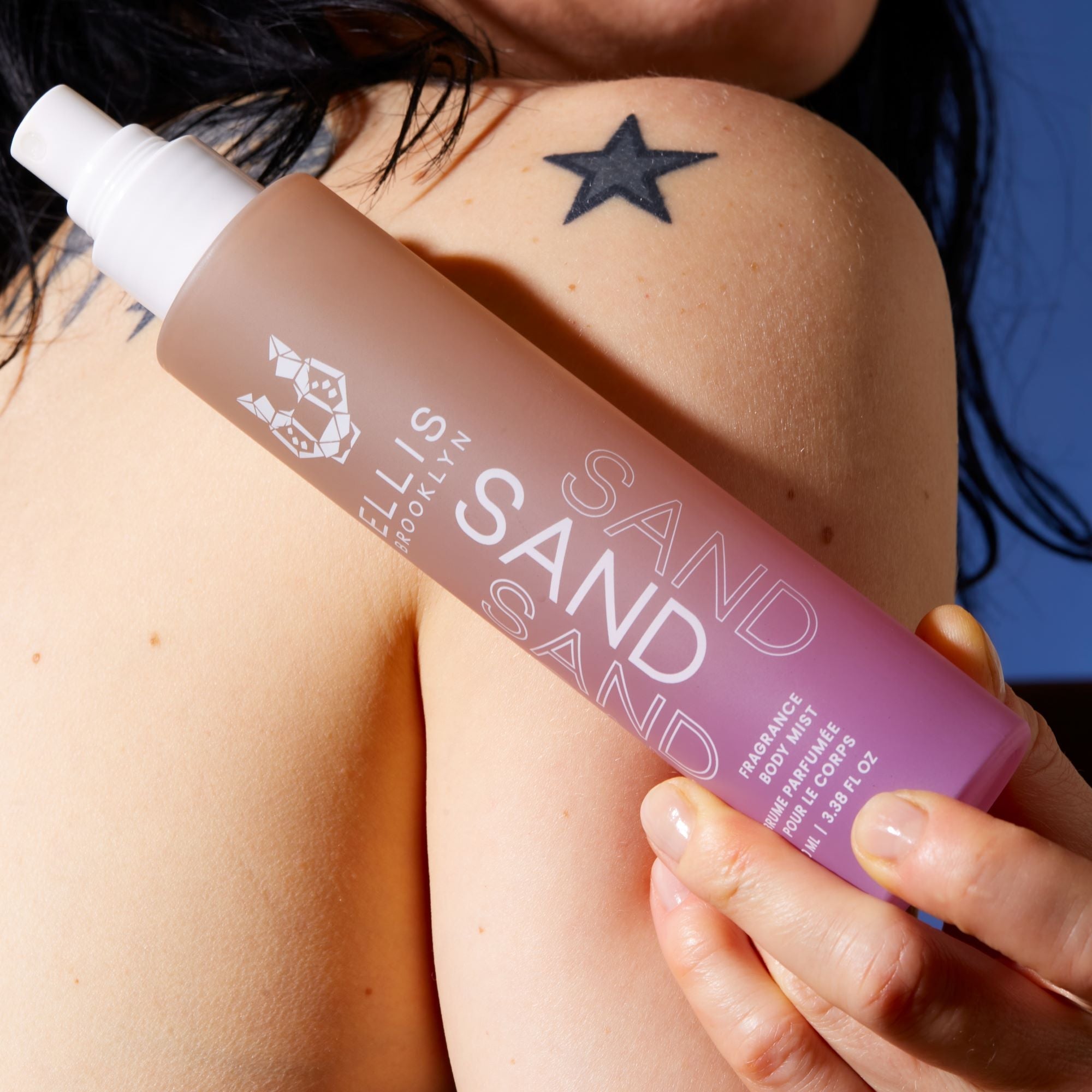 IMAGE 6: MODEL HOLDING SAND FRAGRANCE AND BODY MIST 100ML AGAINST SHOULDER