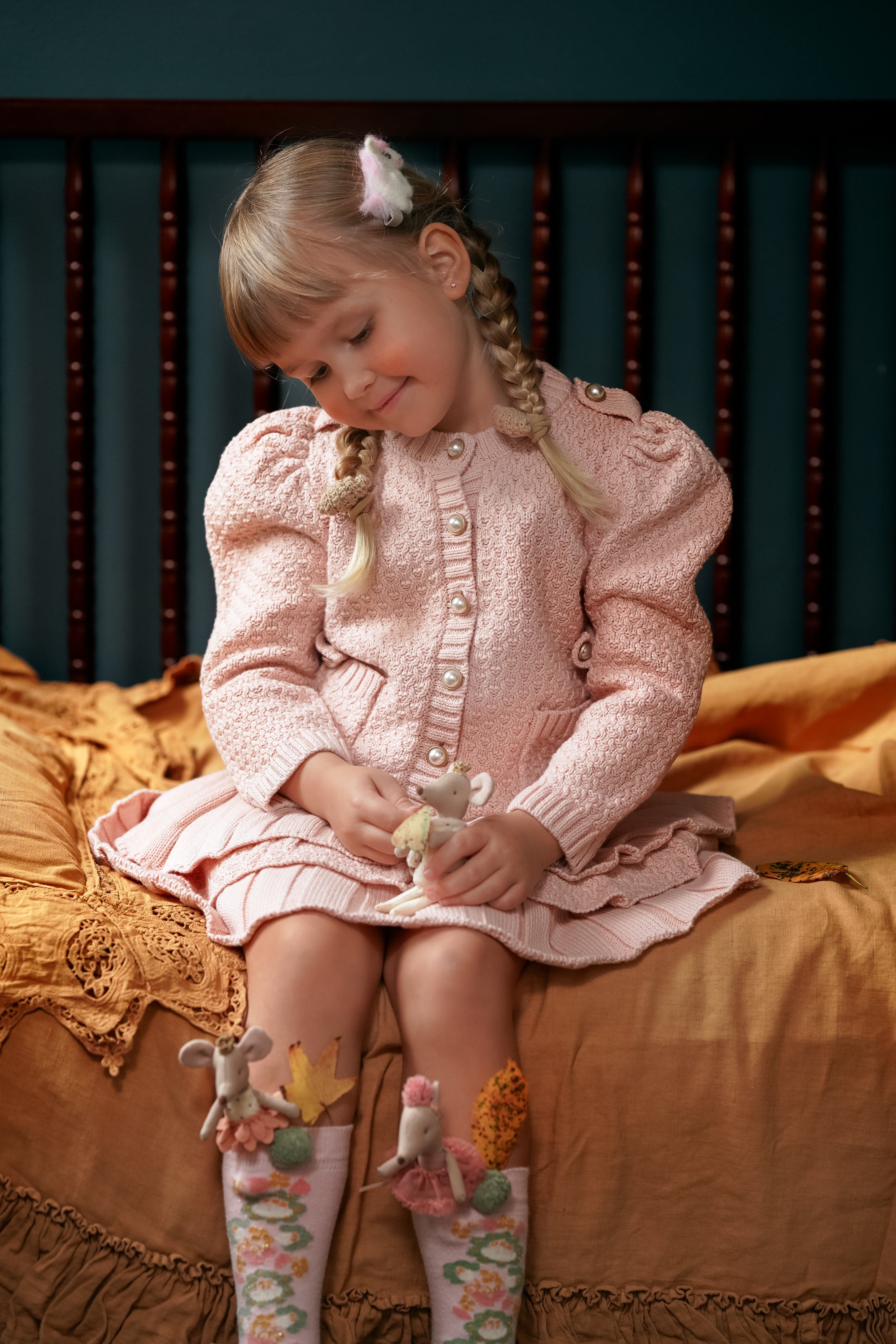 Girl wearing Julie pink knit cotton top and ruffle skirt set while seated, showcasing puff sleeves and feminine knit details