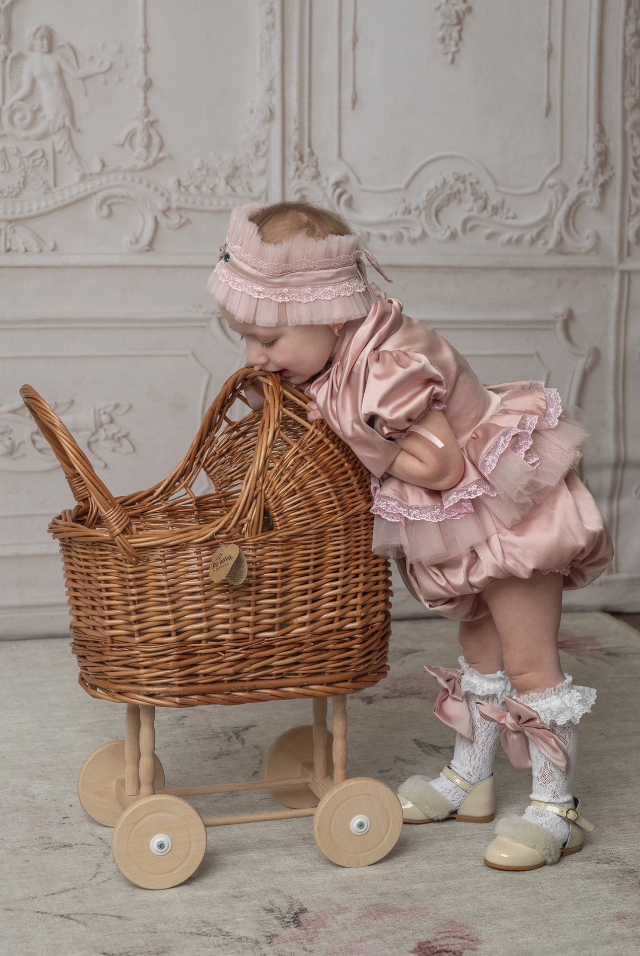 Baby girl in pink ruffle romper with wicker toy cart