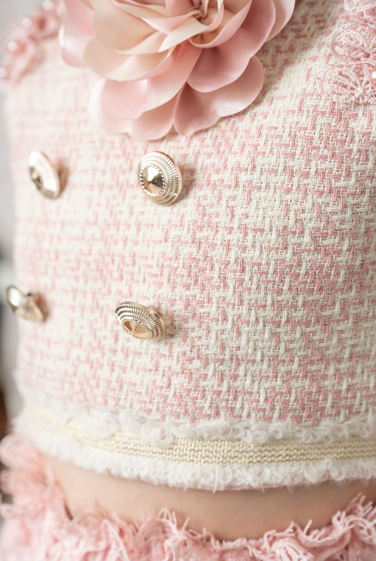 Close up of a pink and beige tweed top with gold button details and a pink floral accent