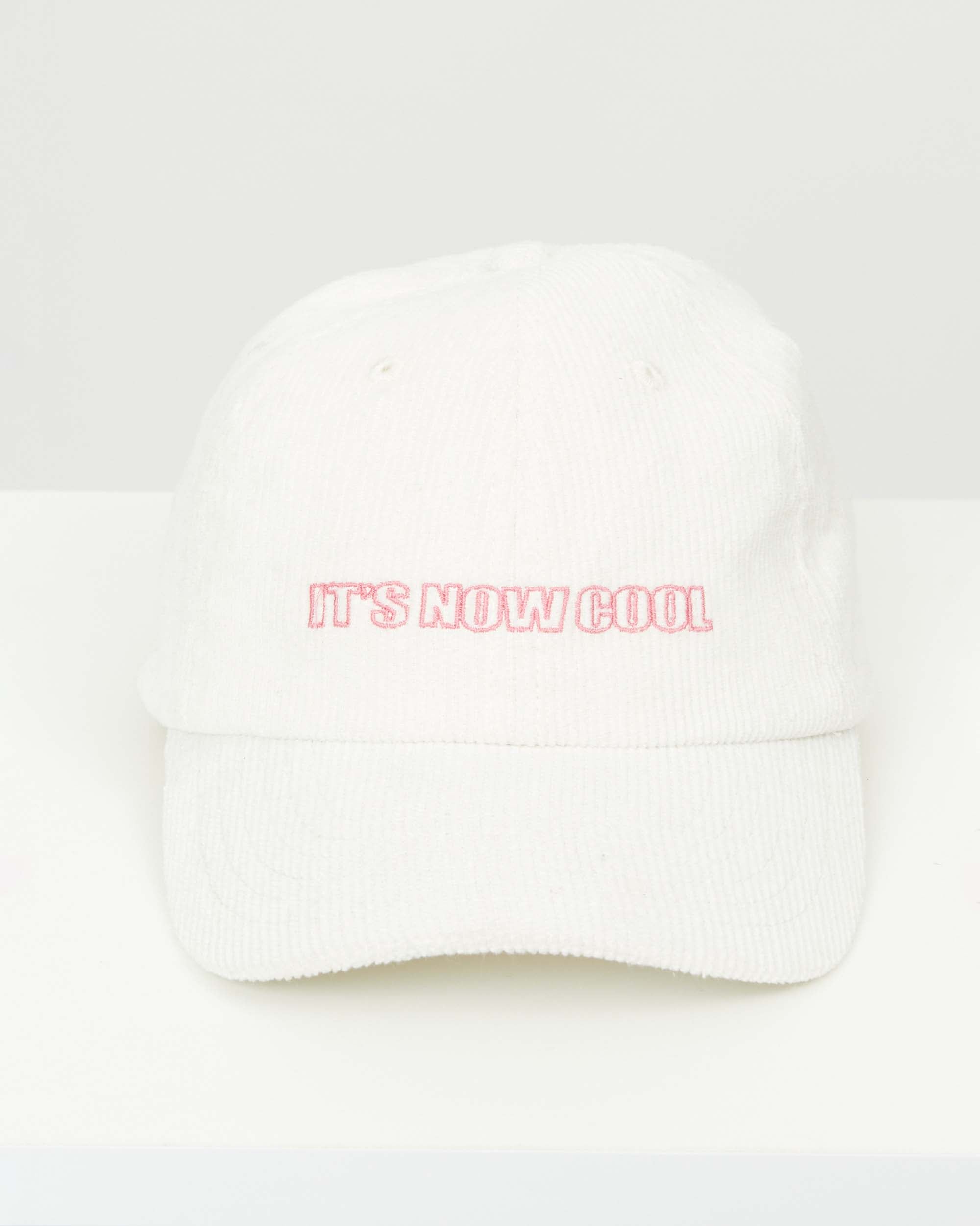 Studio image of the cord cap in white cord, highlighting its "It's Now Cool" embroidery with adjustable back clasp.