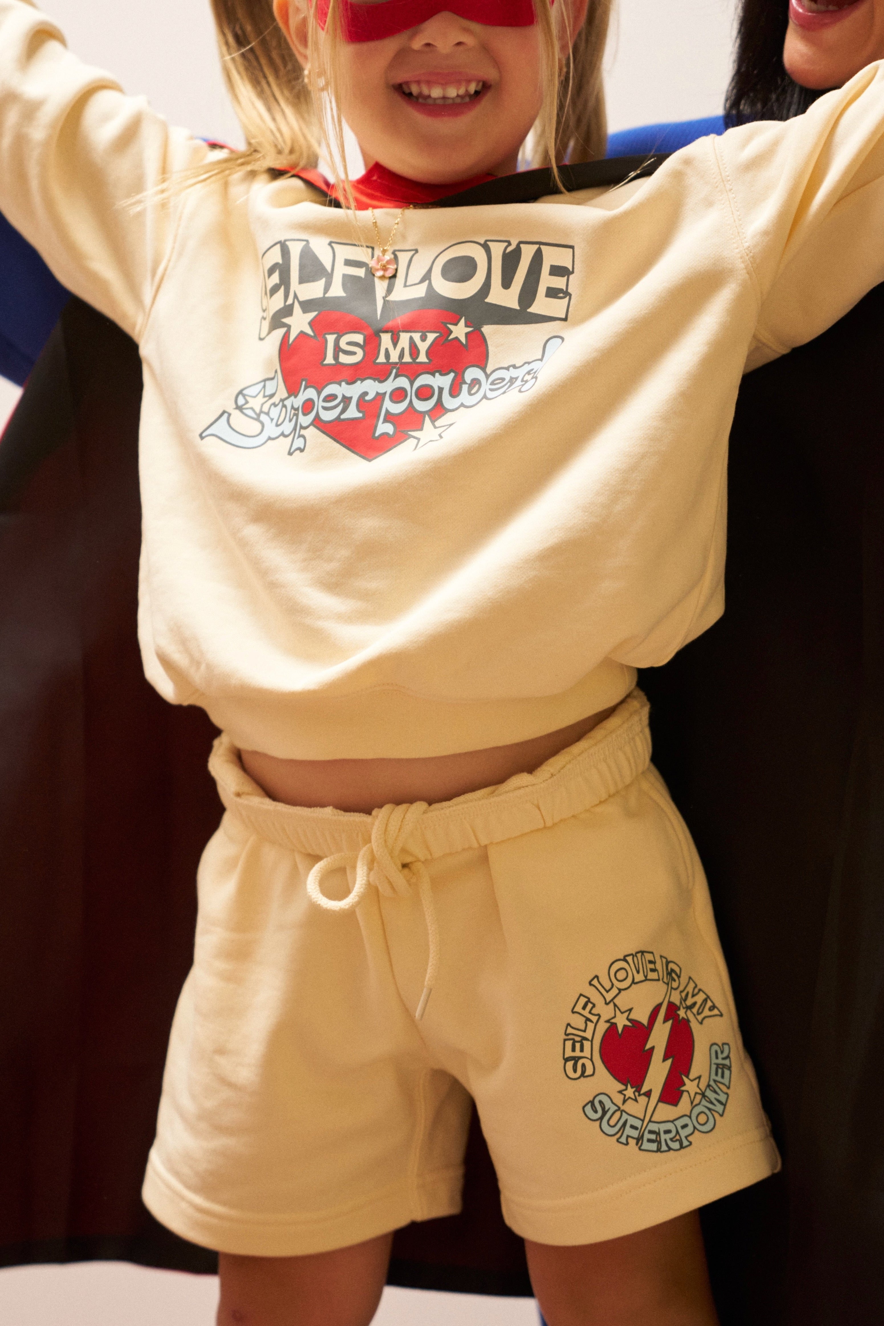 Child wearing a yellow outfit with 'Love is my Superpower' text and superhero cape.