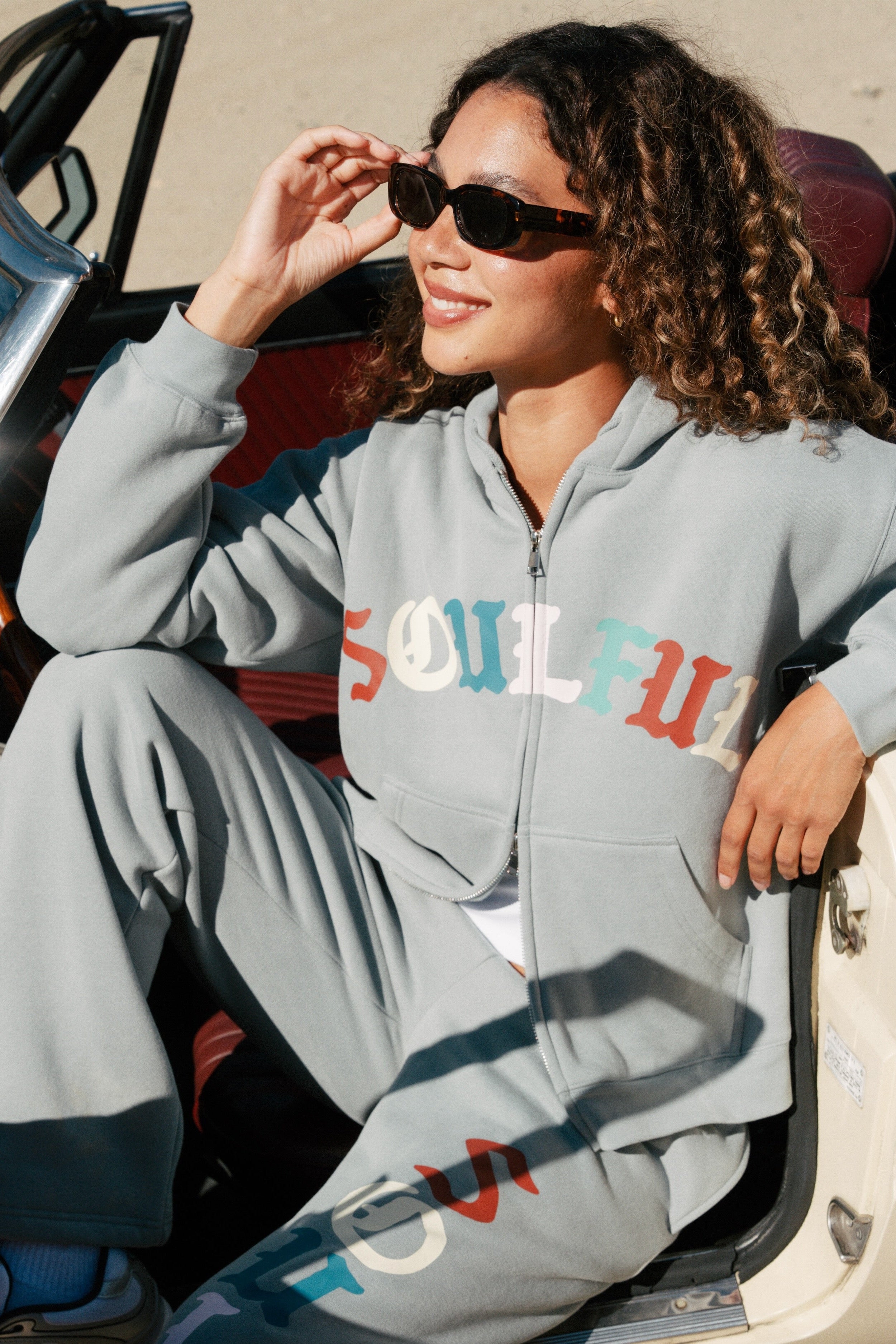 Woman wearing a blue 'Soulful' tracksuit sitting in a car.