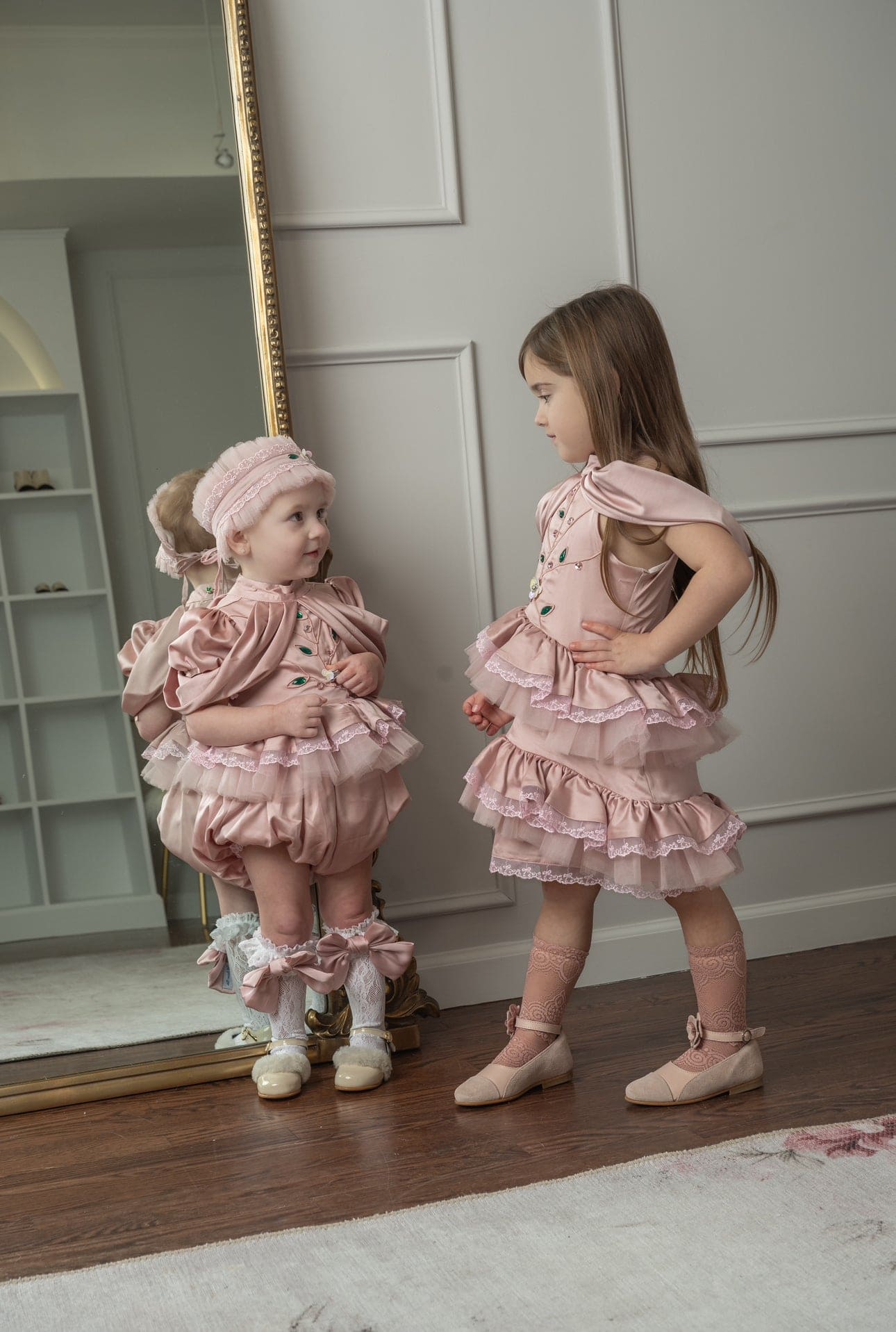 Baby and toddler girls wearing matching pink ruffle lace outfits with satin details