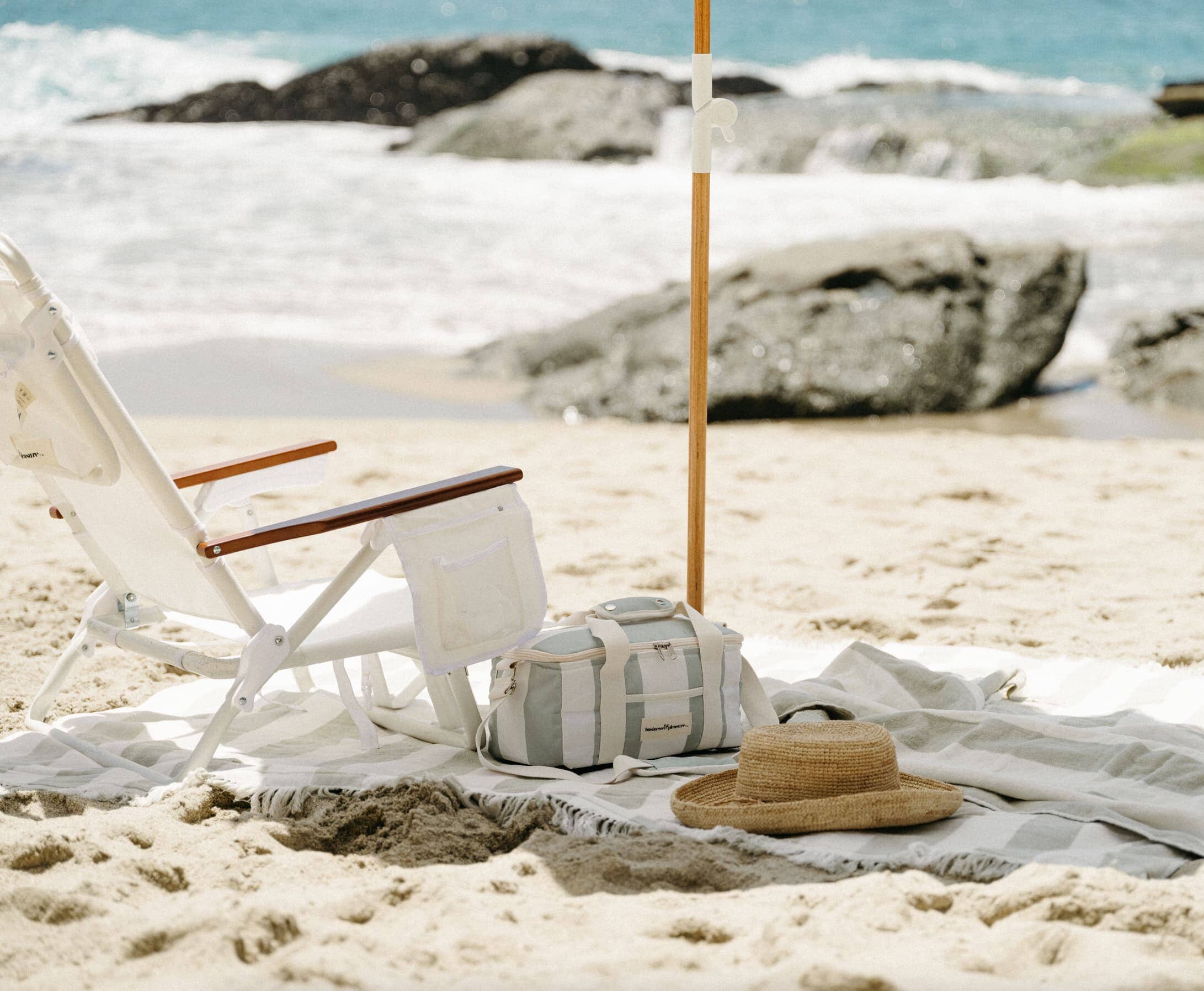 white holiday tommy chair, sage blanket and sage umbrella on a beach